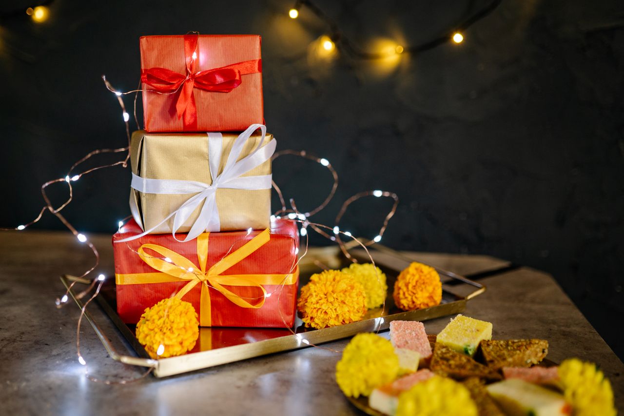 services-01 Colorful wrapped presents on a tray adorned with lights and marigold flowers for Diwali celebration.